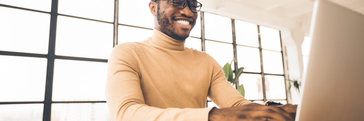 Black man wearing glasses typing on a laptop while working on digital skills.